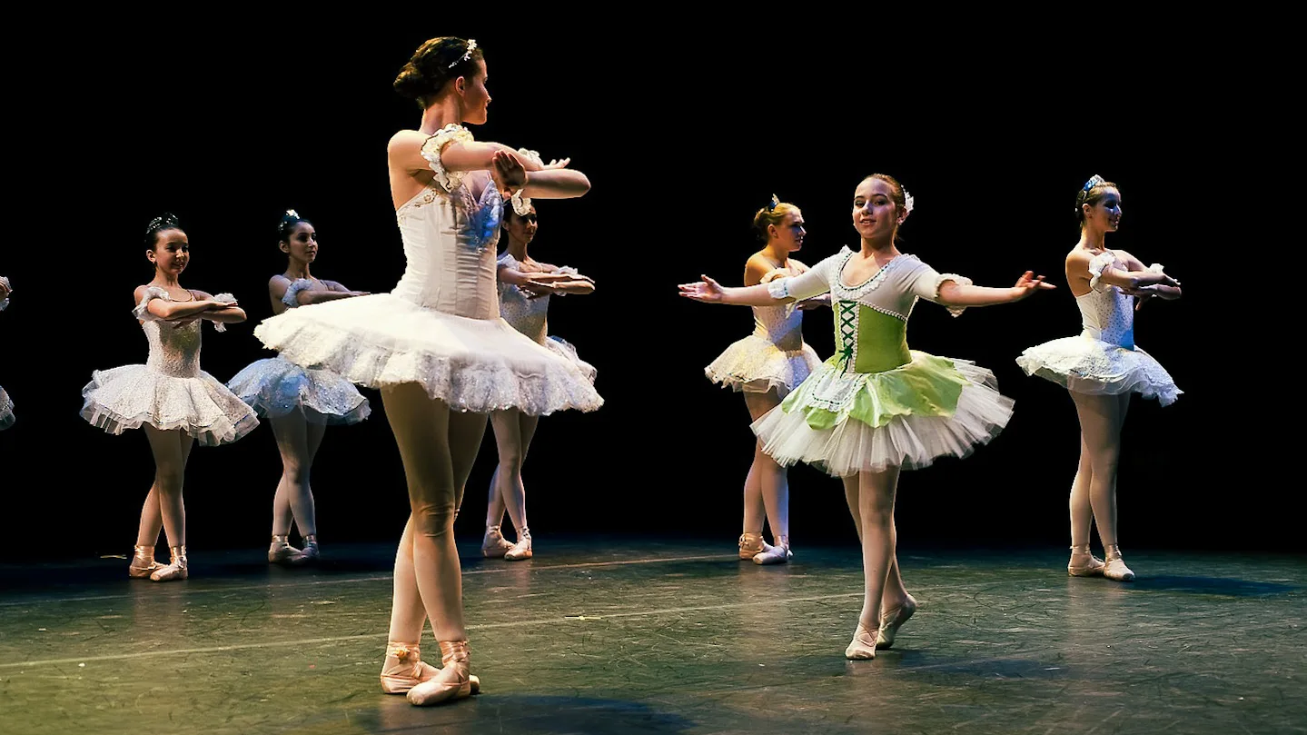 Nika dancers in tutus performing on a darkened stage